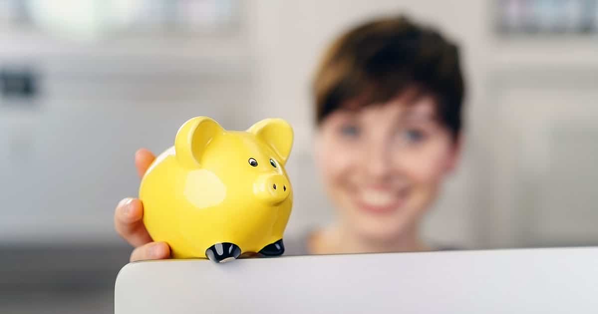 Woman smiling at piggybank sitting on computer screen